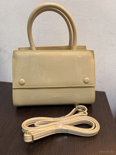Элегантная женская сумка светло-бежевого цвета с лаковой поверхностью.